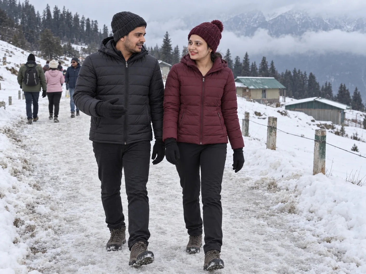 Nav and Vandana walking along a snowy path lined with fence posts in January 2026, other walkers ahead and green-roofed buildings below.