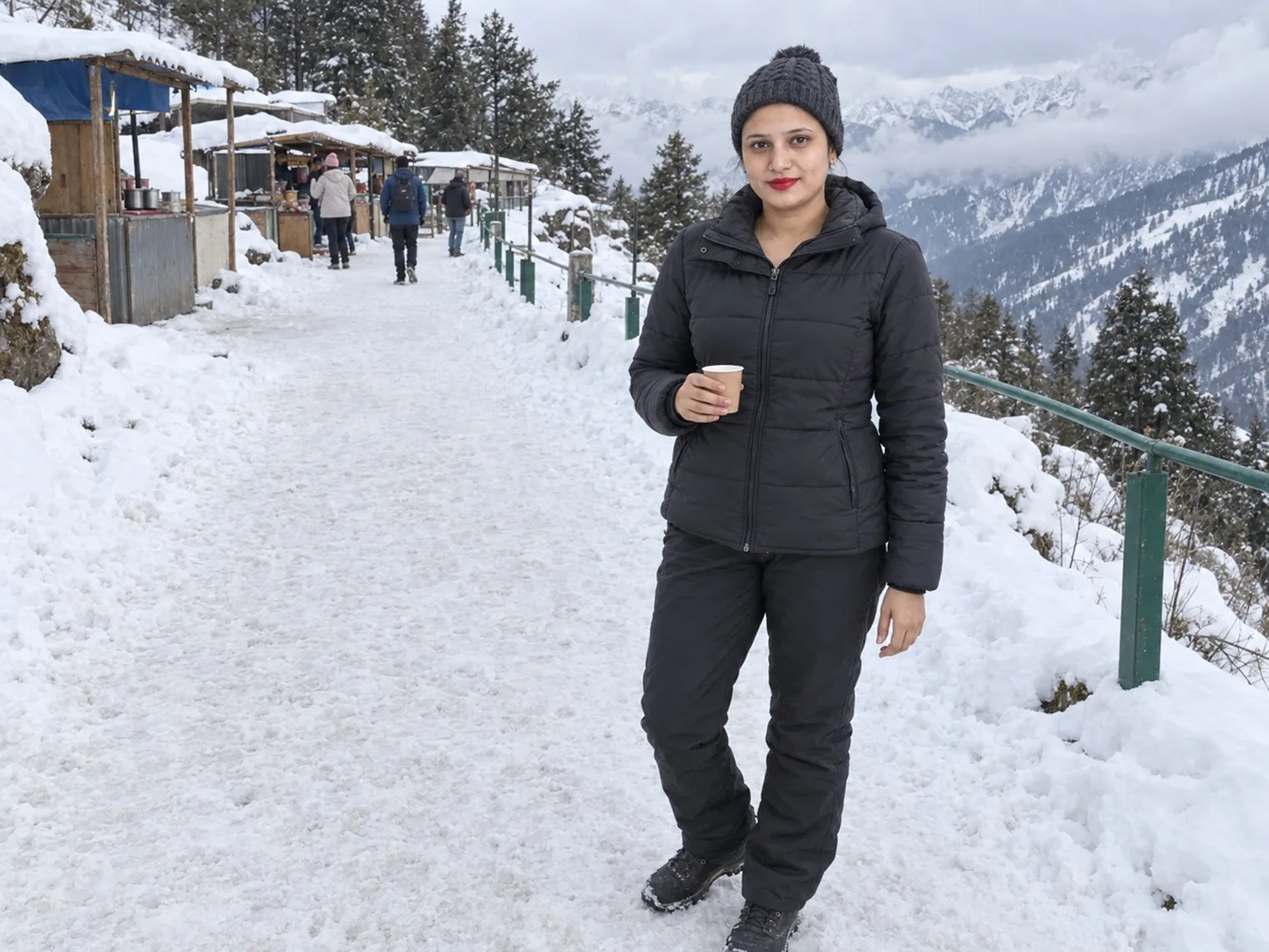 Vandana holding a paper cup on a trodden snow path in January 2026, a row of small stalls with blue awnings behind her.