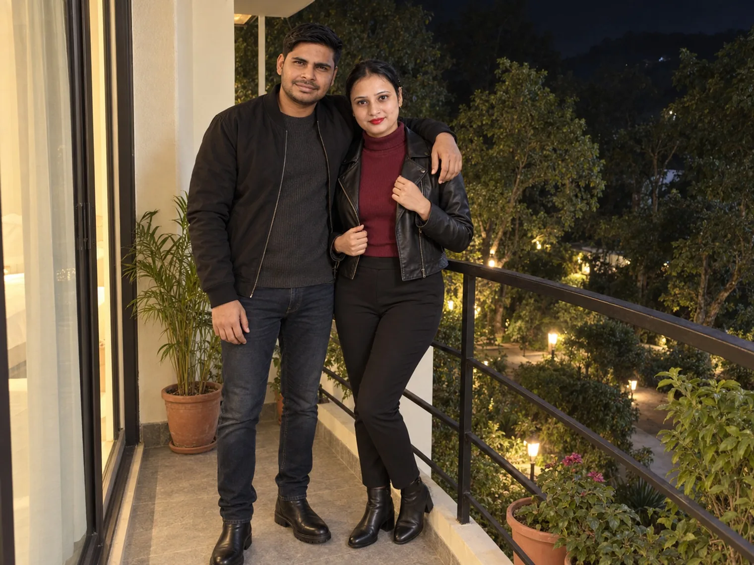 Nav and Vandana standing at a balcony rail at night, garden lamps and trees below them.