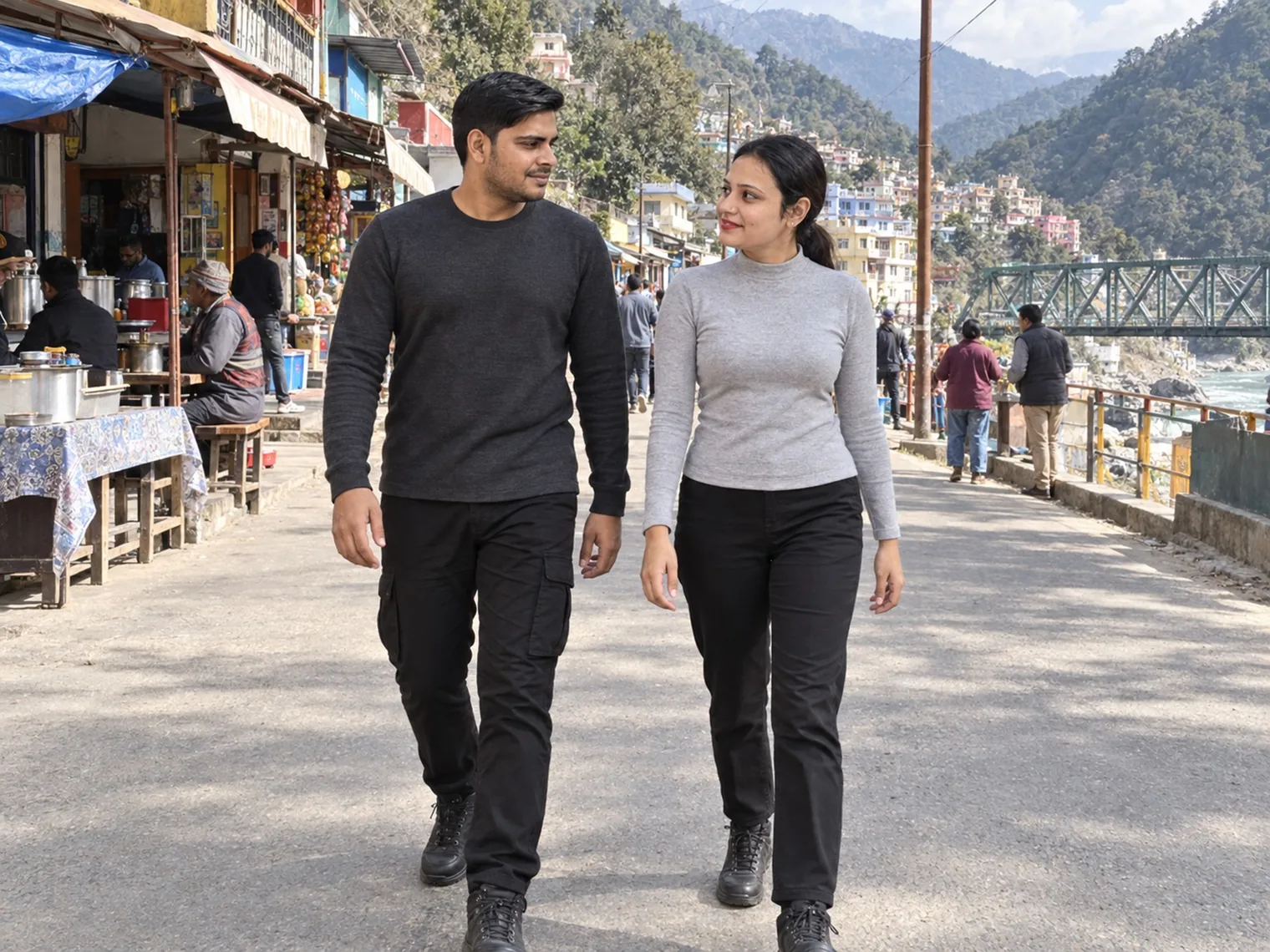 Nav and Vandana walking down a narrow market street lined with shops, a river and a bridge beyond.