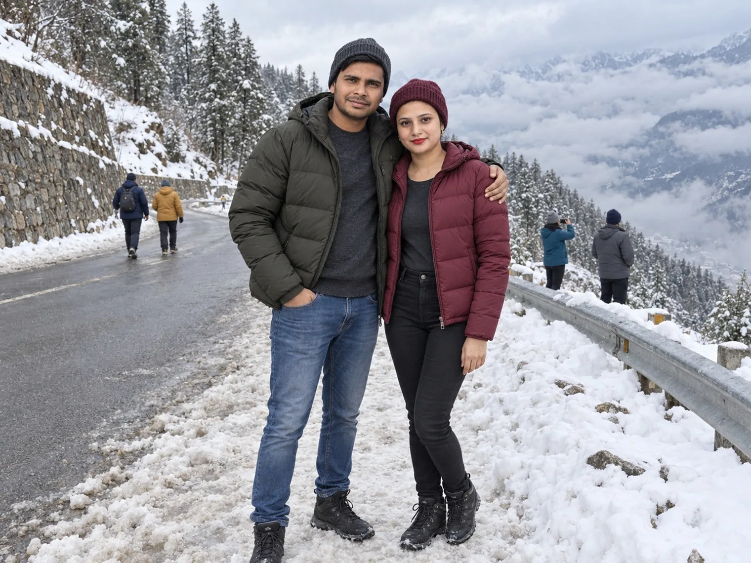 Nav and Vandana beside a snowy guardrail on the mountain road, other people walking and cloud filling the valley.